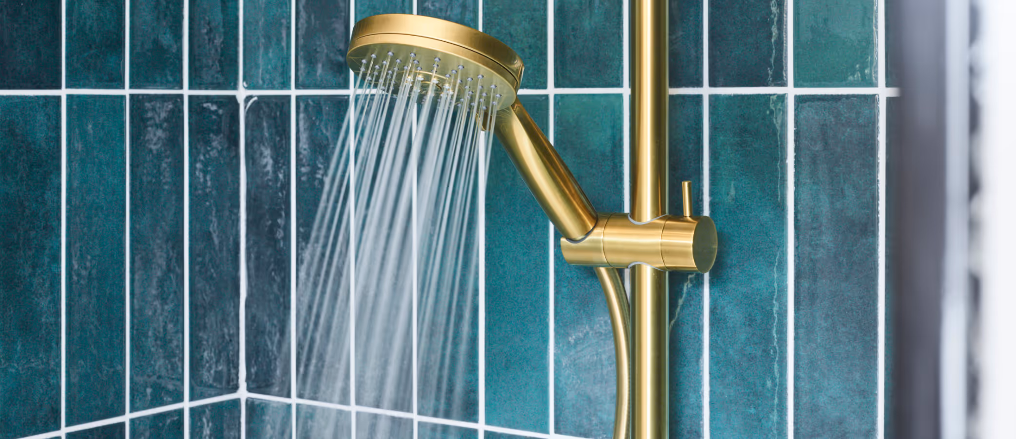 Gouden handdouche die waterstraal uitstraalt tegen groene geglazuurde tegels.