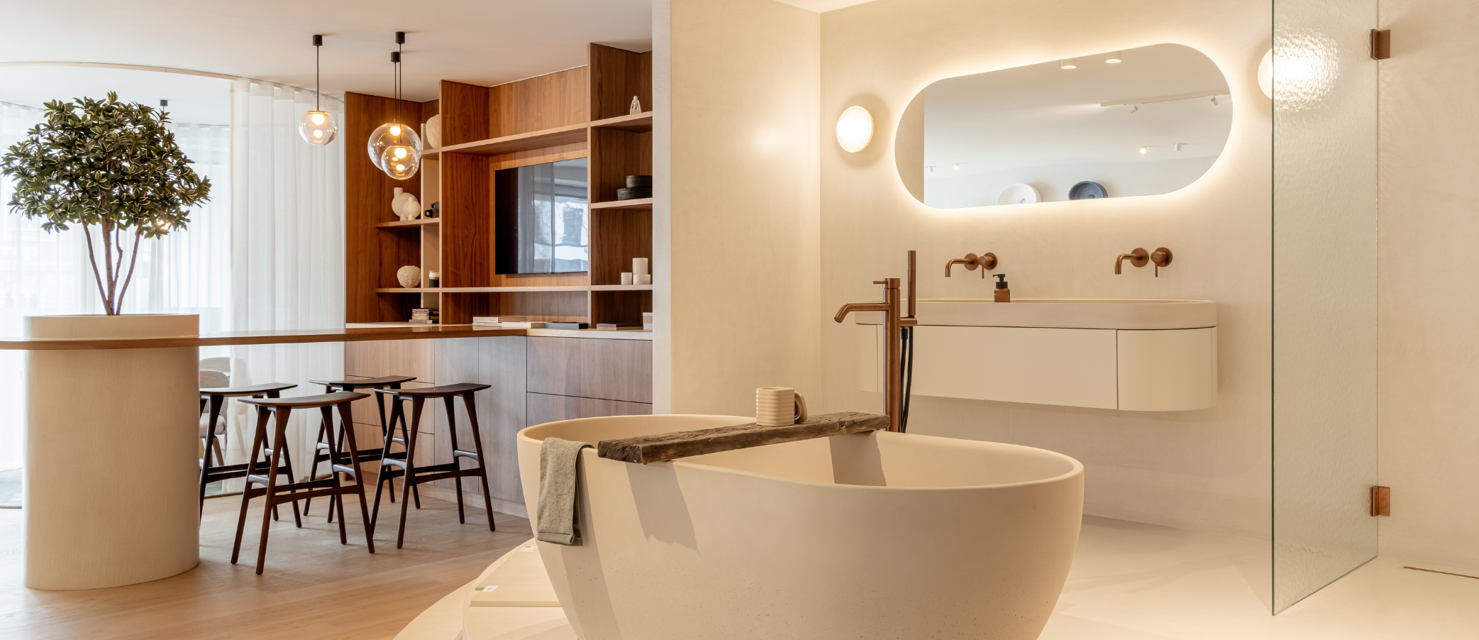 Moderne badkamer met vrijstaand ovaal bad, houten krukken bij een bar, en een verlichte ronde spiegel aan een beige wand.