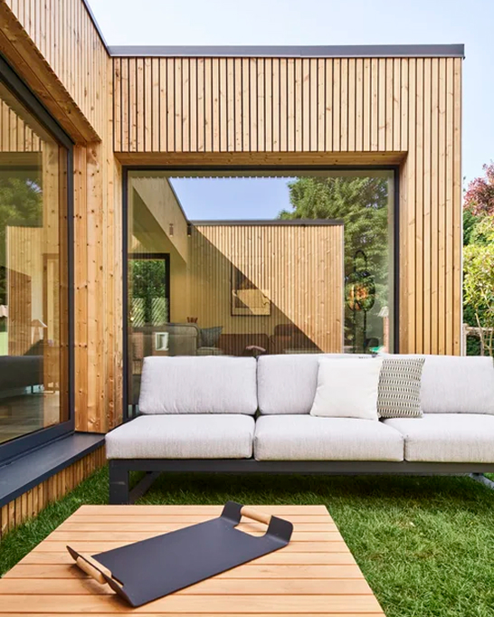 Een foto van een woning die voorzien is van een houtskelet opbouw, plat dak en houten gevelbekleding.