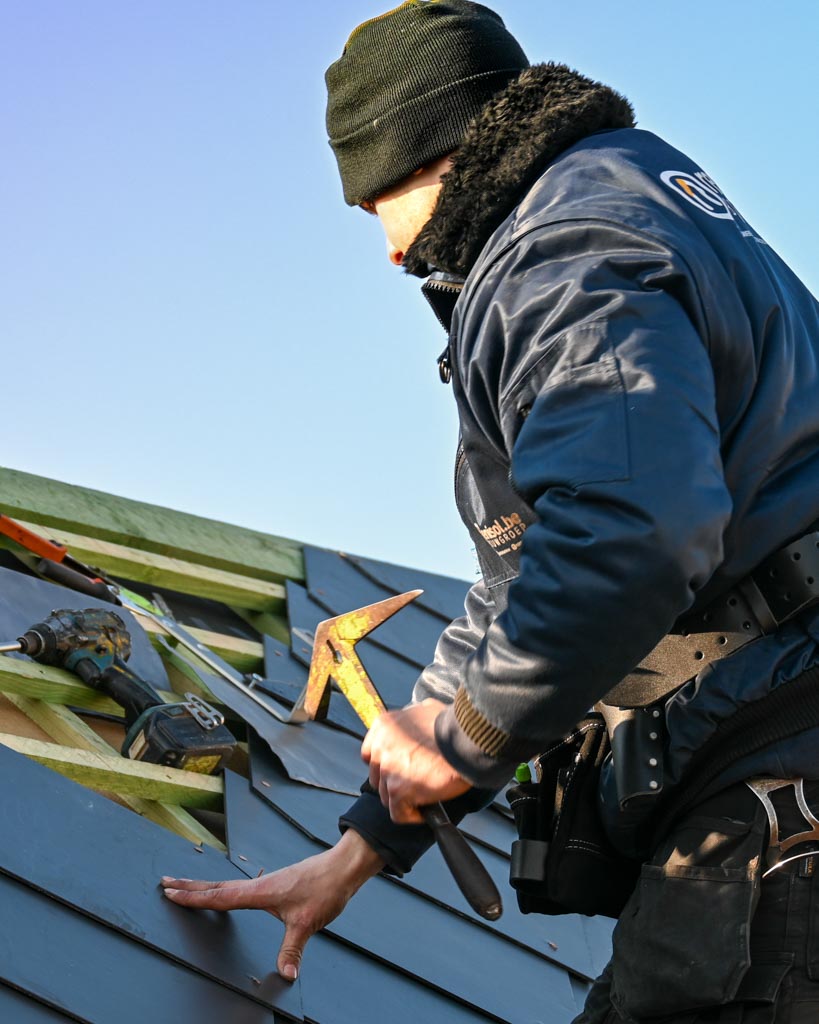 Een foto van één van onze dakwerkers die leien aan het kloppen is op een hellend dak.
