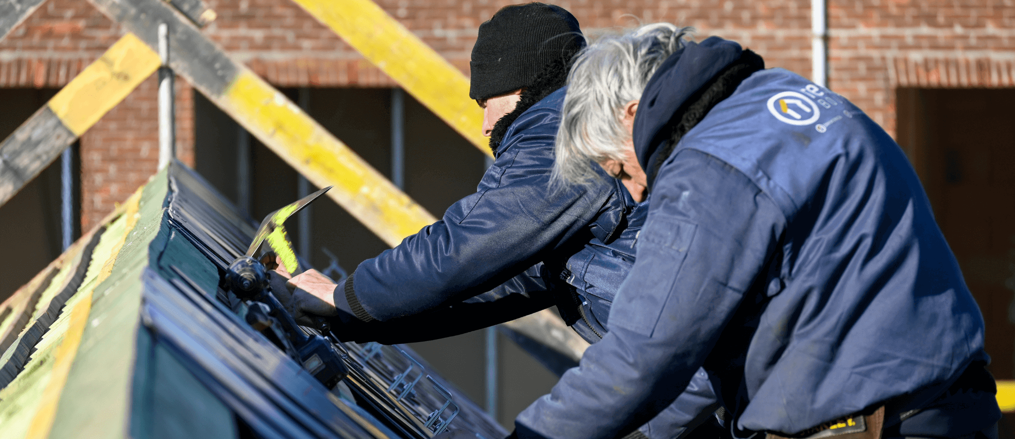 Een foto van onze arbeiders die leien aan het kloppen zijn op het hellend dak.