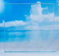 Transparent glass block reflecting a blue sky with white clouds.