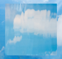 Transparent glass block reflecting a blue sky with white clouds.