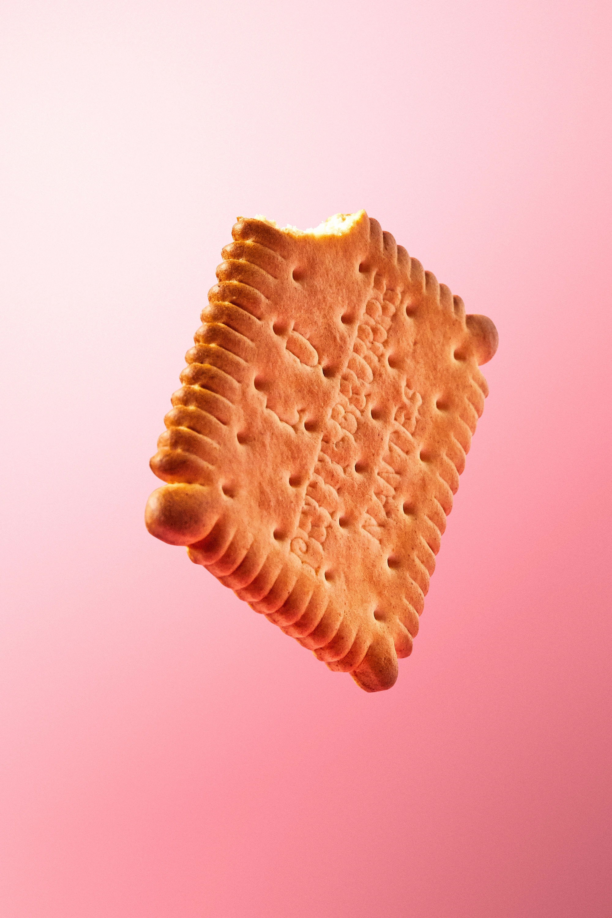 Close-up of a rectangular biscuit with a bite taken out of one corner against a pink gradient background.