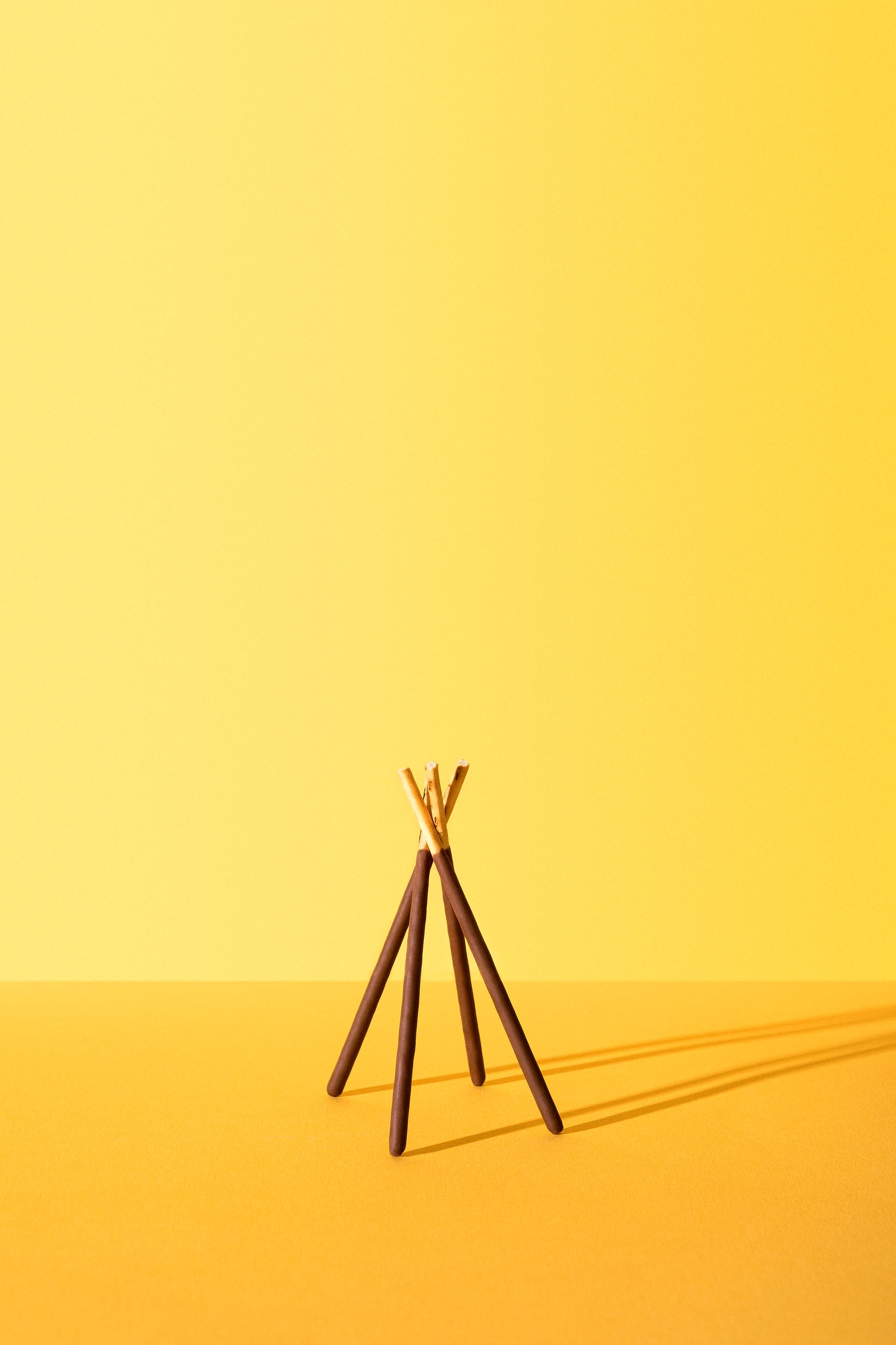 Three chocolate-dipped biscuit sticks standing upright and leaning together on a yellow surface with a yellow background.