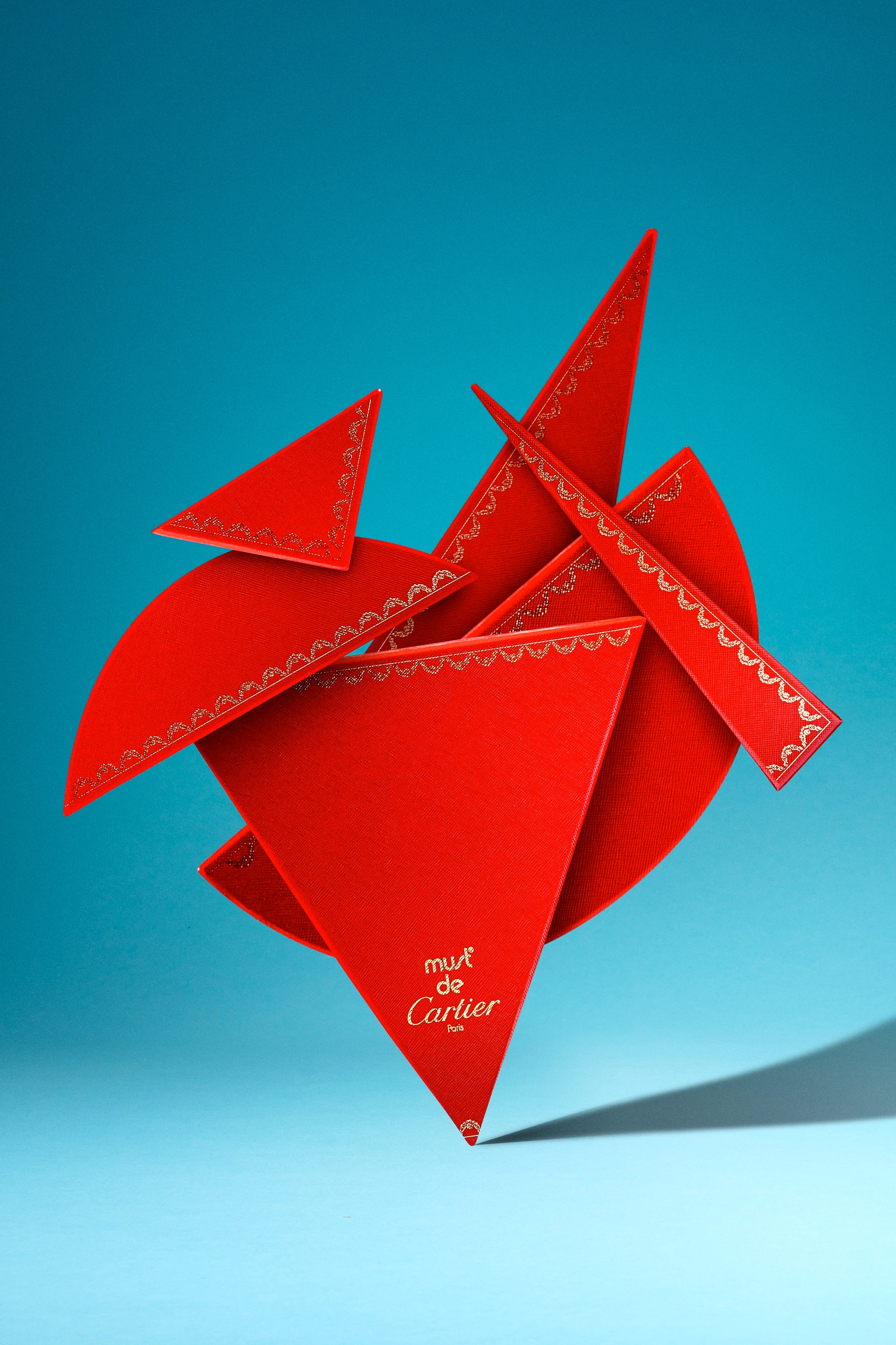 Abstract arrangement of red geometric shapes with gold decorative details and 'must de Cartier Paris' text on a blue background.