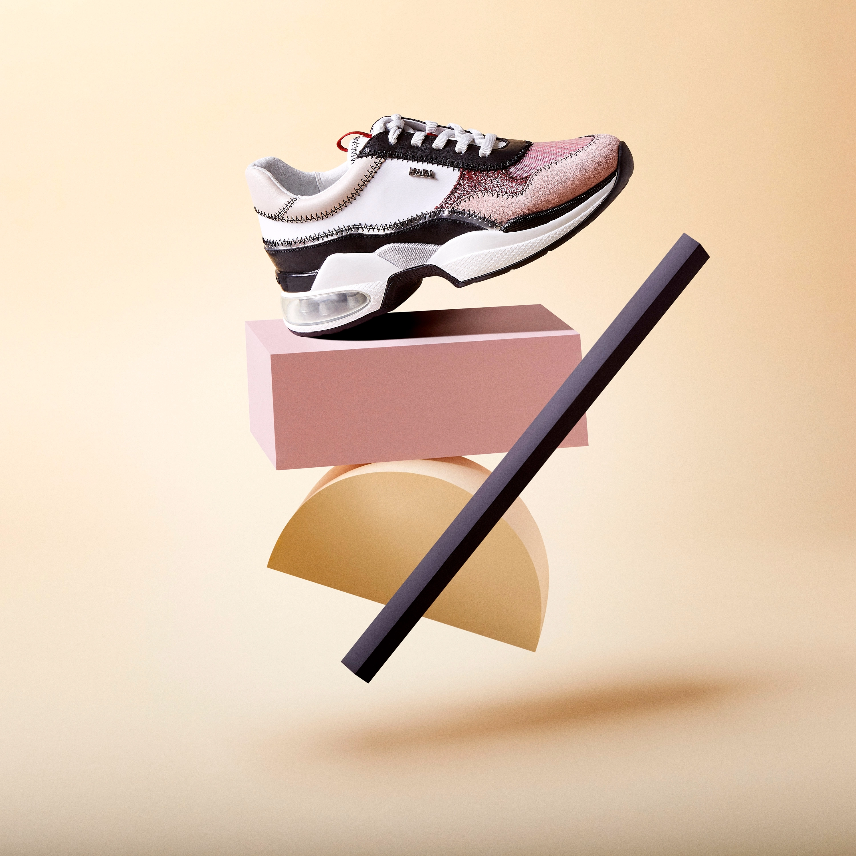 Stylish sneaker in white, black, and pink with a visible air cushion sole, balanced on geometric shapes against a beige background.