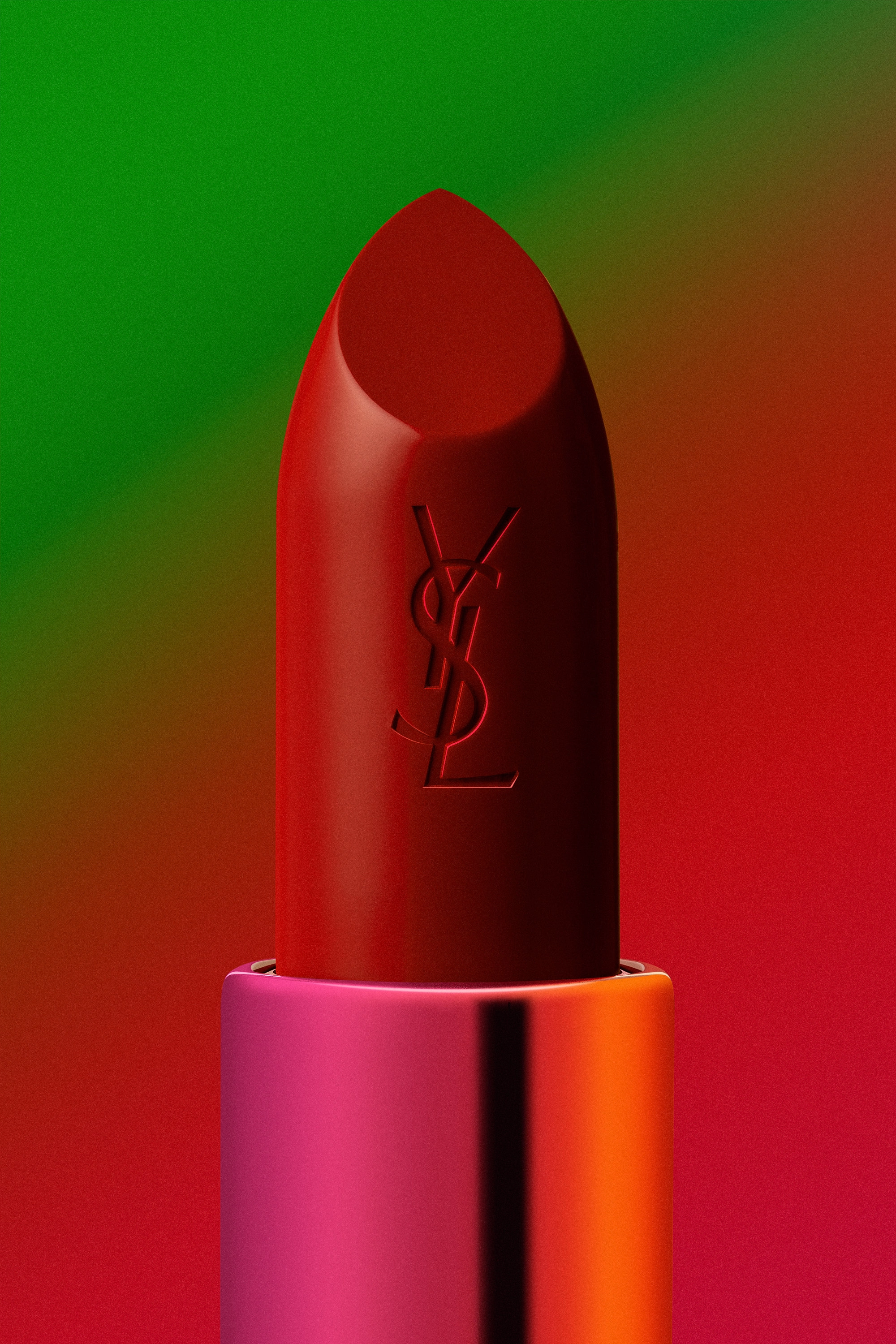Close-up of a red YSL lipstick with a pink and orange metallic base against a green and red gradient background.