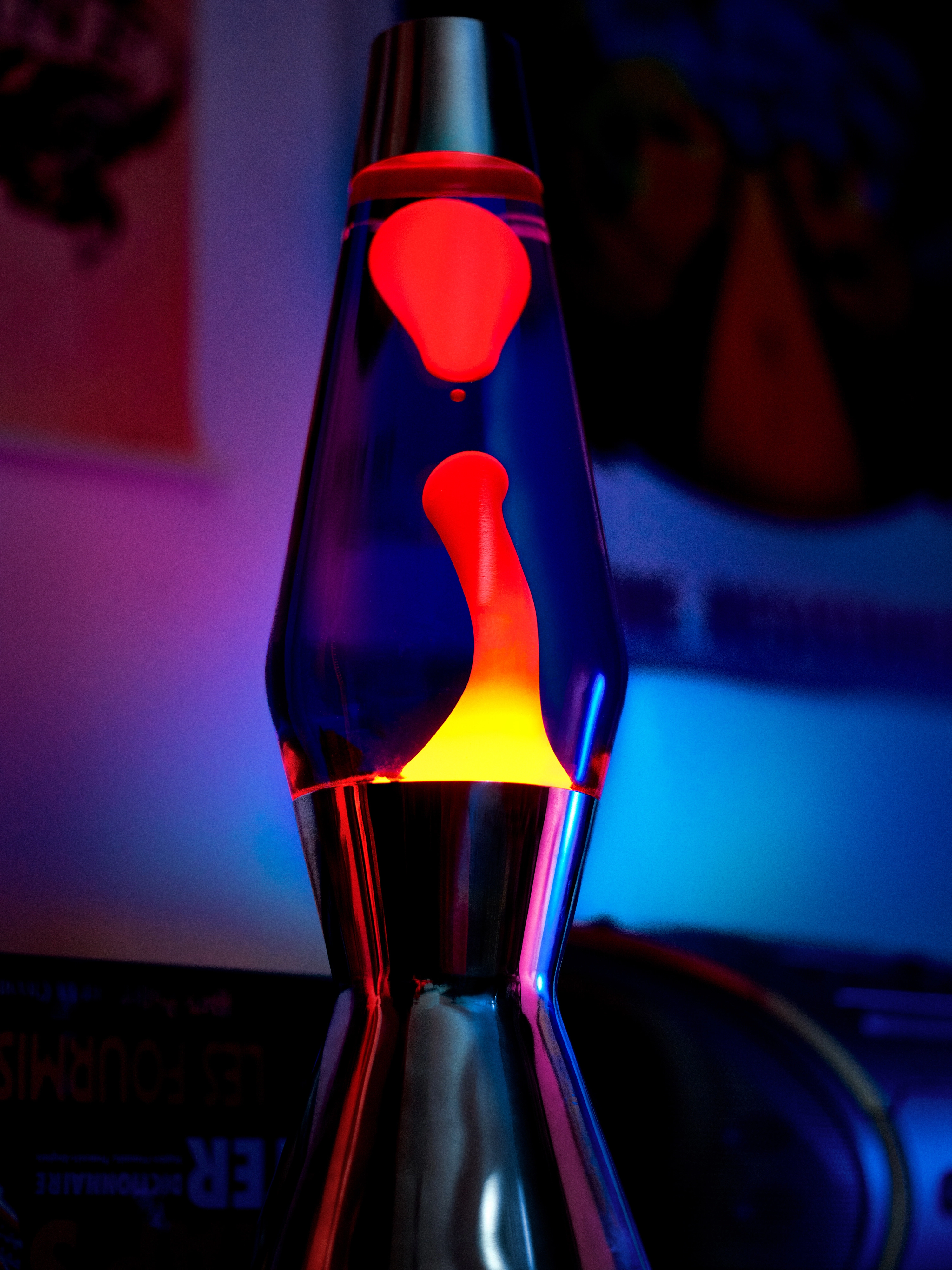 Close-up of a lava lamp with red wax shapes suspended in yellow and blue liquid under colorful ambient lighting.