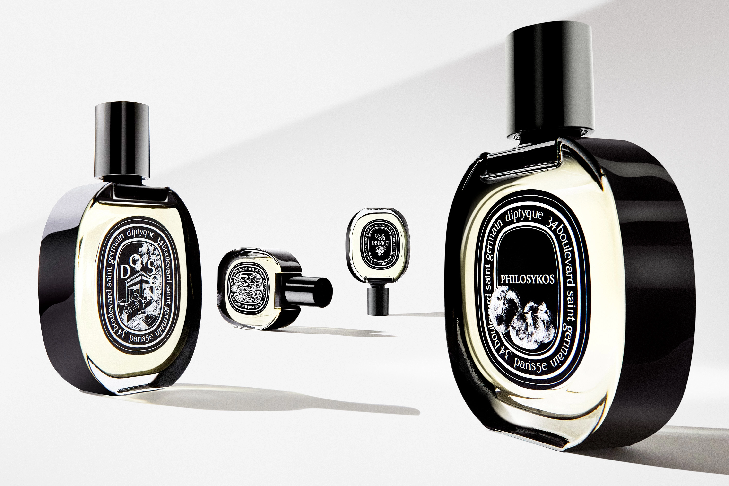 Four Diptyque perfume bottles with black caps and detailed black and white labels on a white surface.