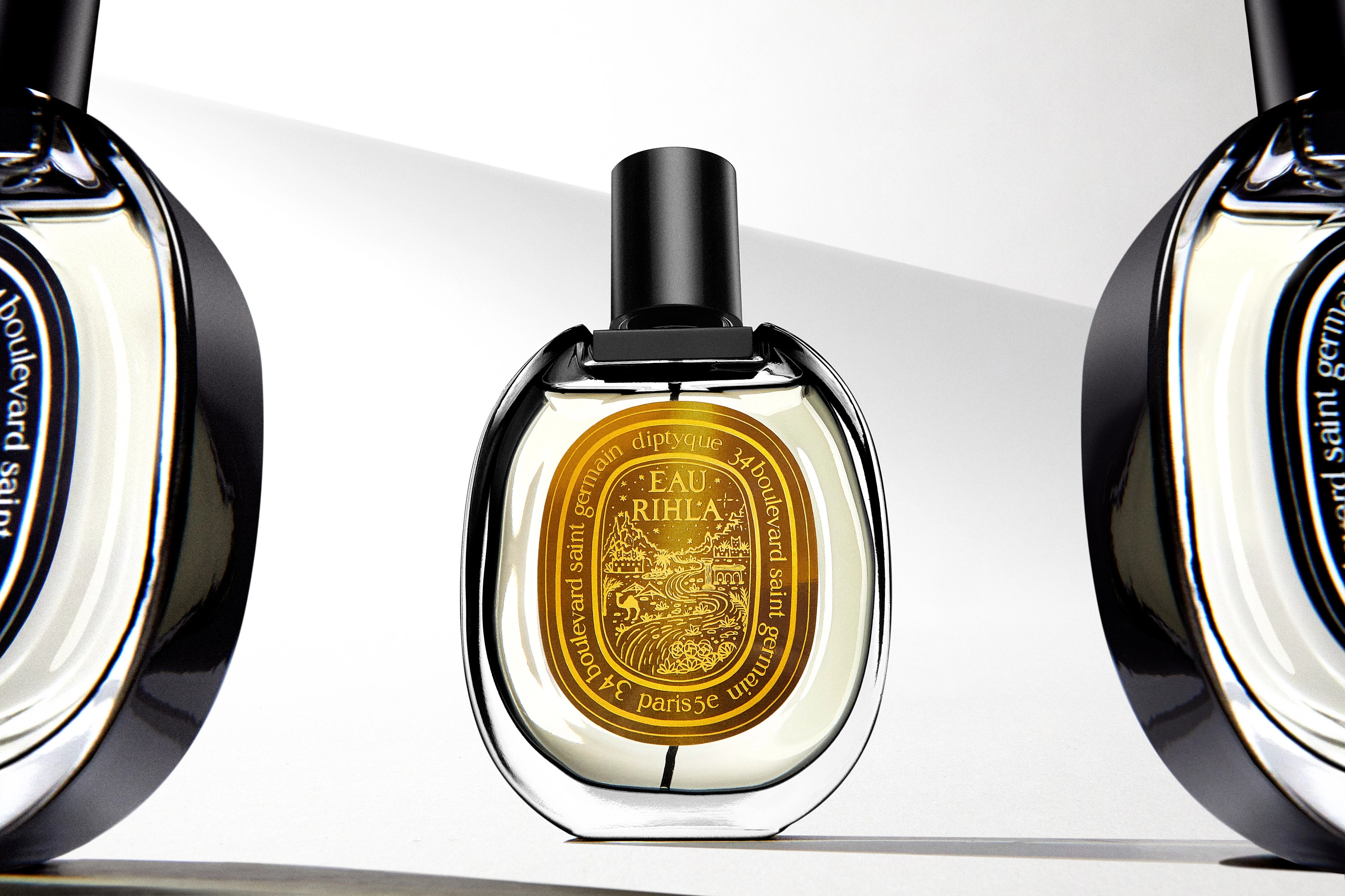 Bottle of Diptyque Eau Rhla perfume with a golden label standing between two partially visible bottles.