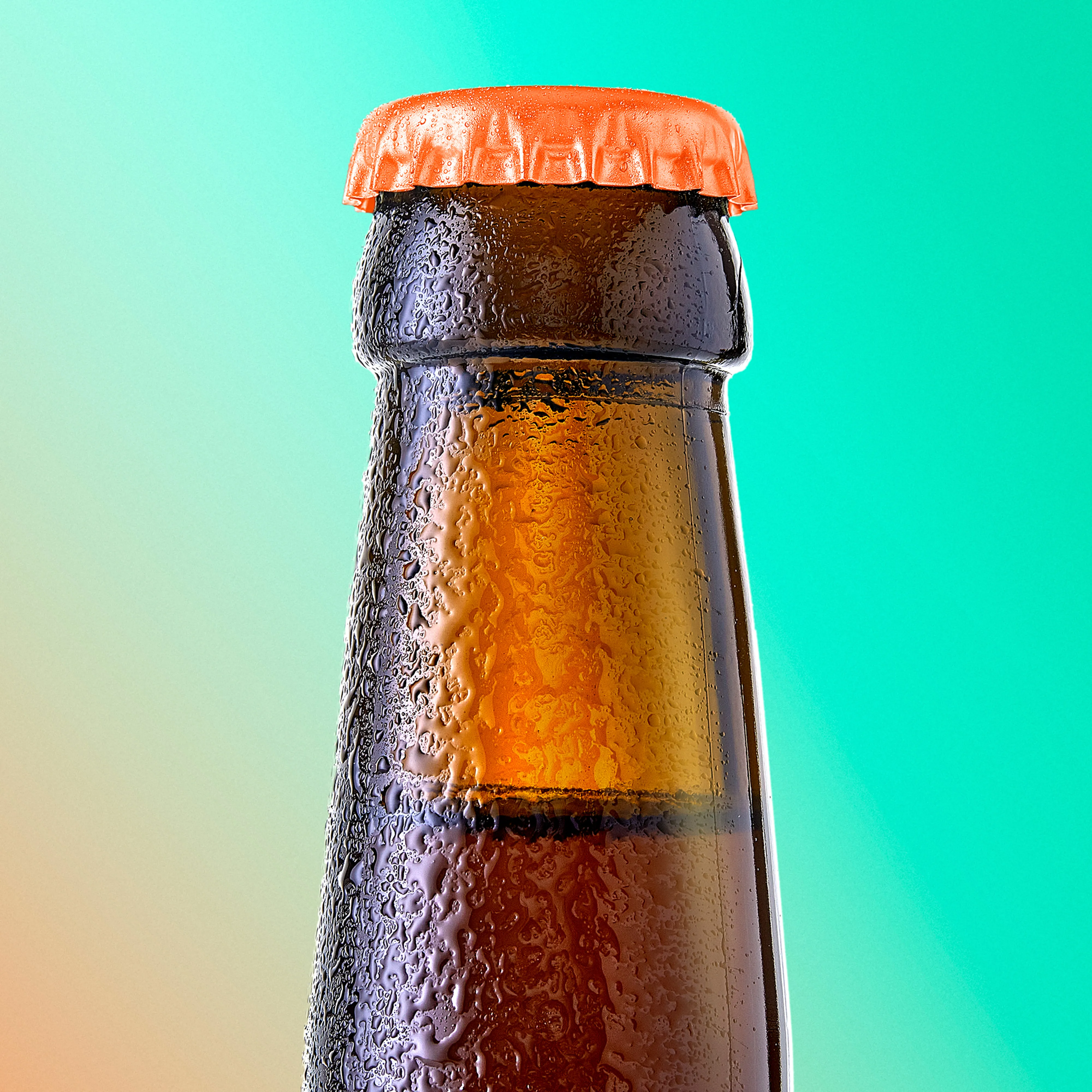 Close-up of the top of a brown glass bottle with an orange bottle cap and condensation droplets.