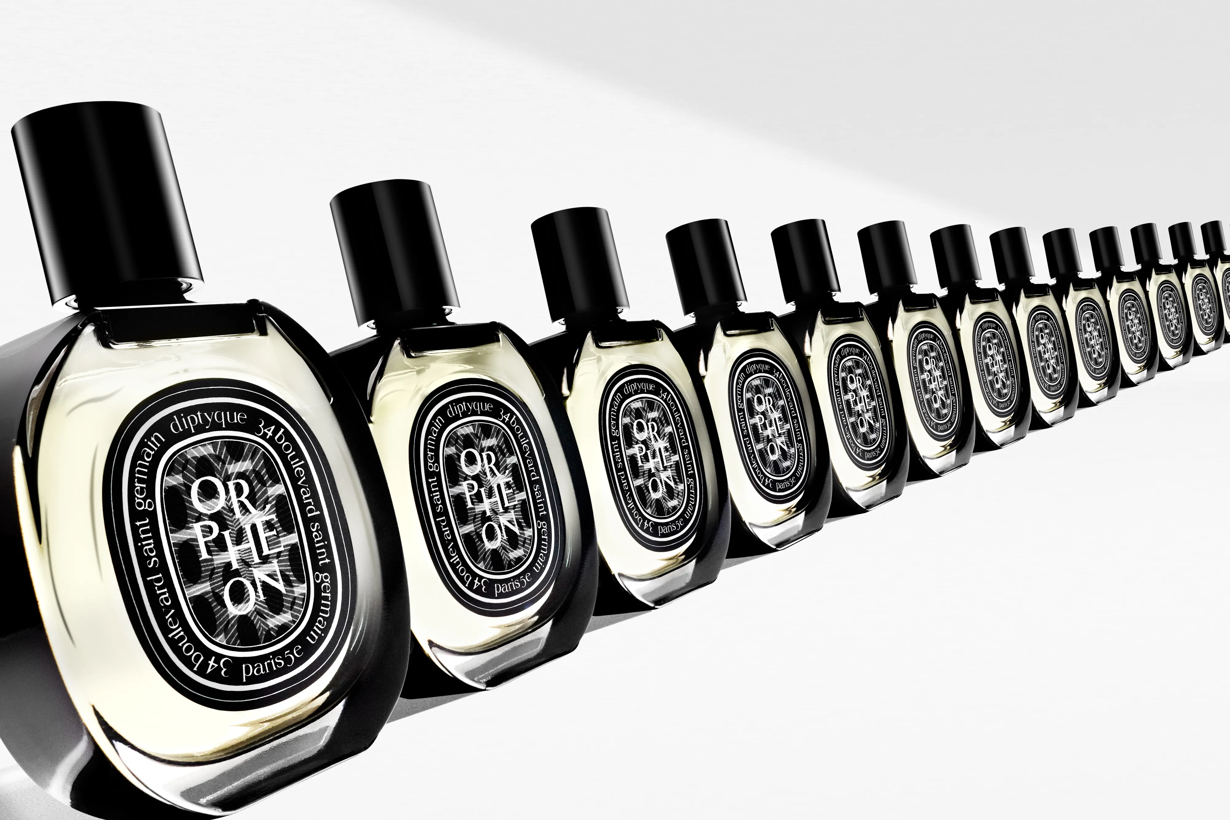 Row of Diptyque Orphéon perfume bottles with black caps arranged diagonally on a white surface.