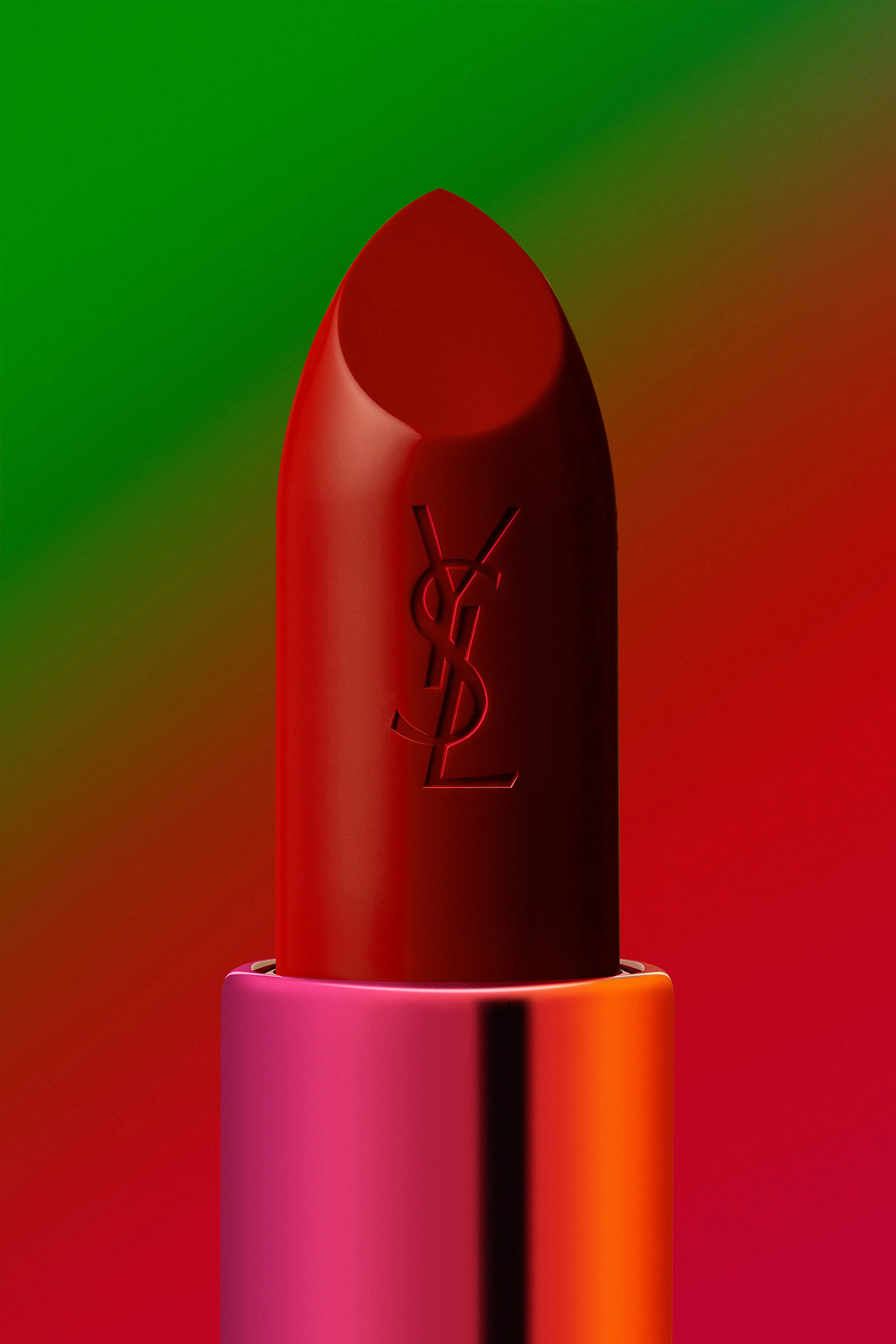 Close-up of a red Yves Saint Laurent lipstick with a metallic pink and orange case against a red and green gradient background.
