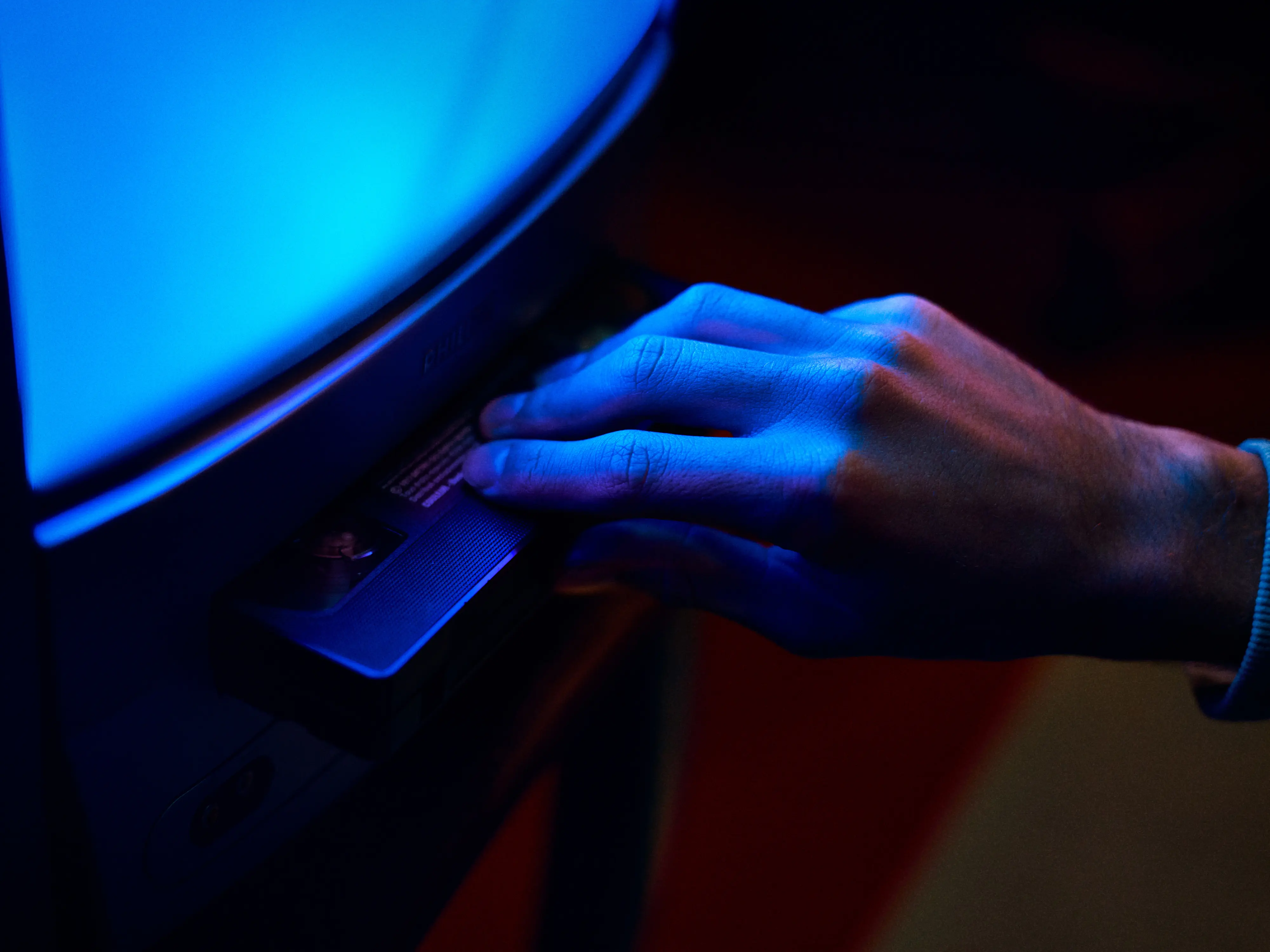 Close-up of a young person’s face illuminated by red and blue light, looking thoughtfully to the side.