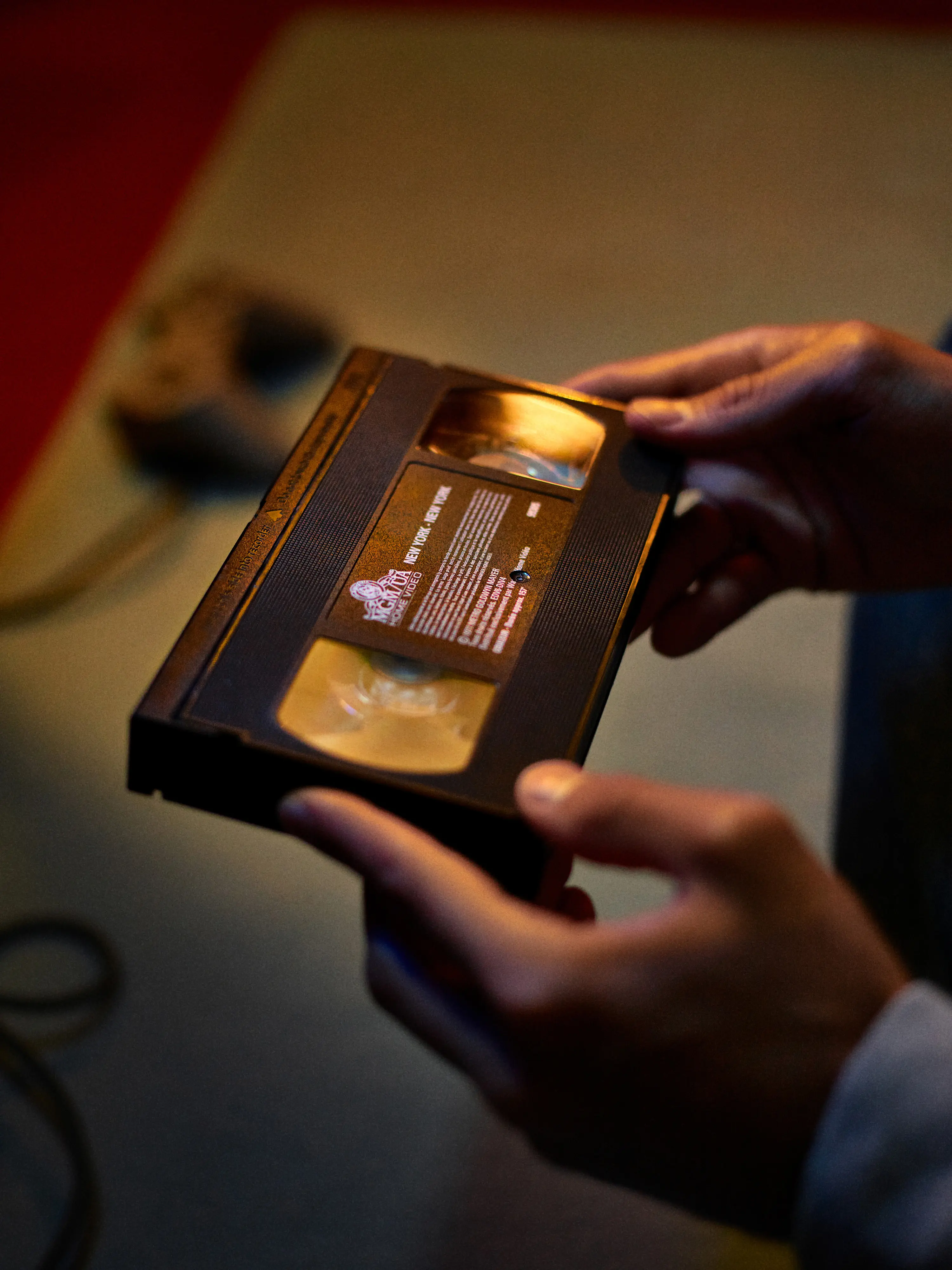 Close-up of a glossy black rectangular object with illuminated Yves Saint Laurent logo in red and pink gradient on a dark red background.