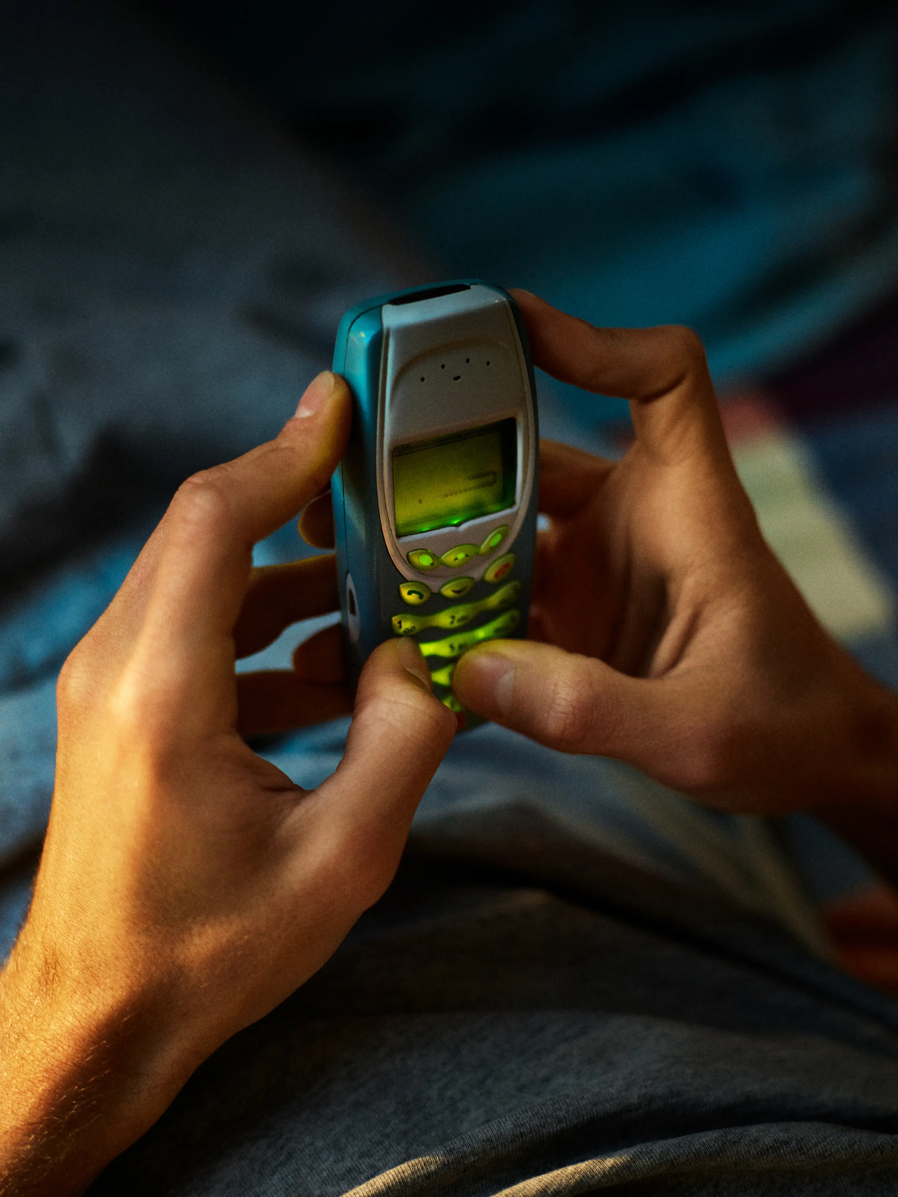 Young man with long hair illuminated by red and purple lighting looking upward thoughtfully in a dark environment.