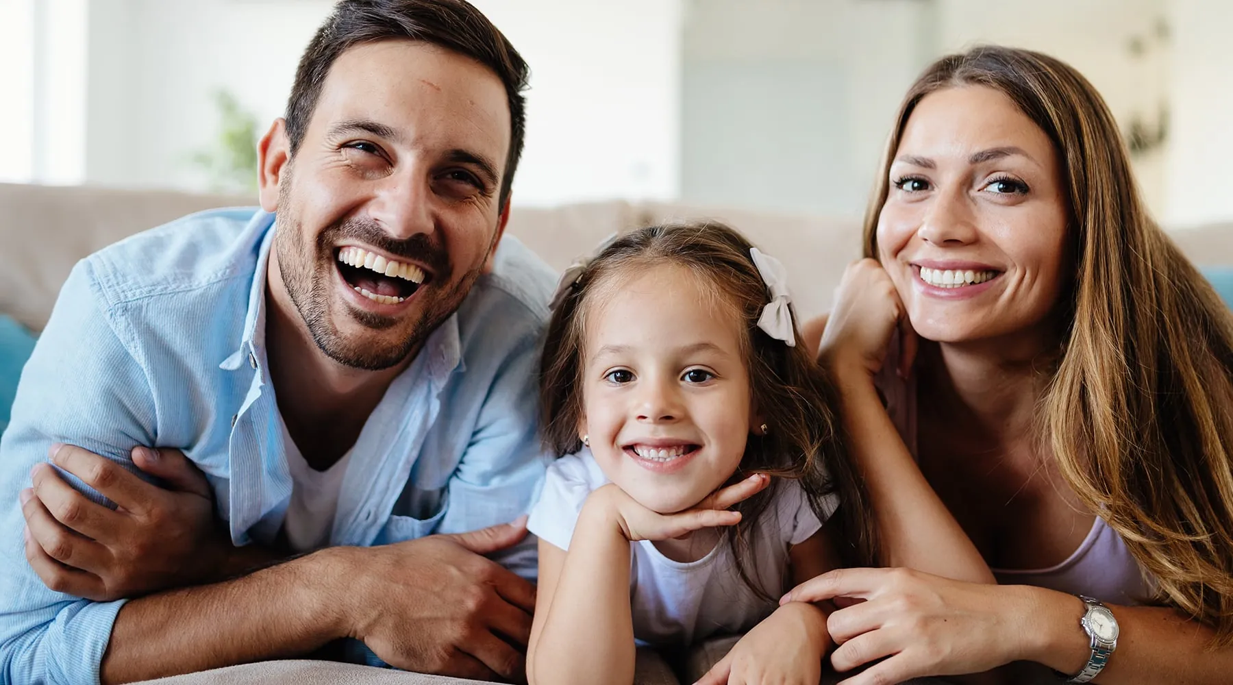 Smiling family of father, mother, and daughter lying on a couch together.