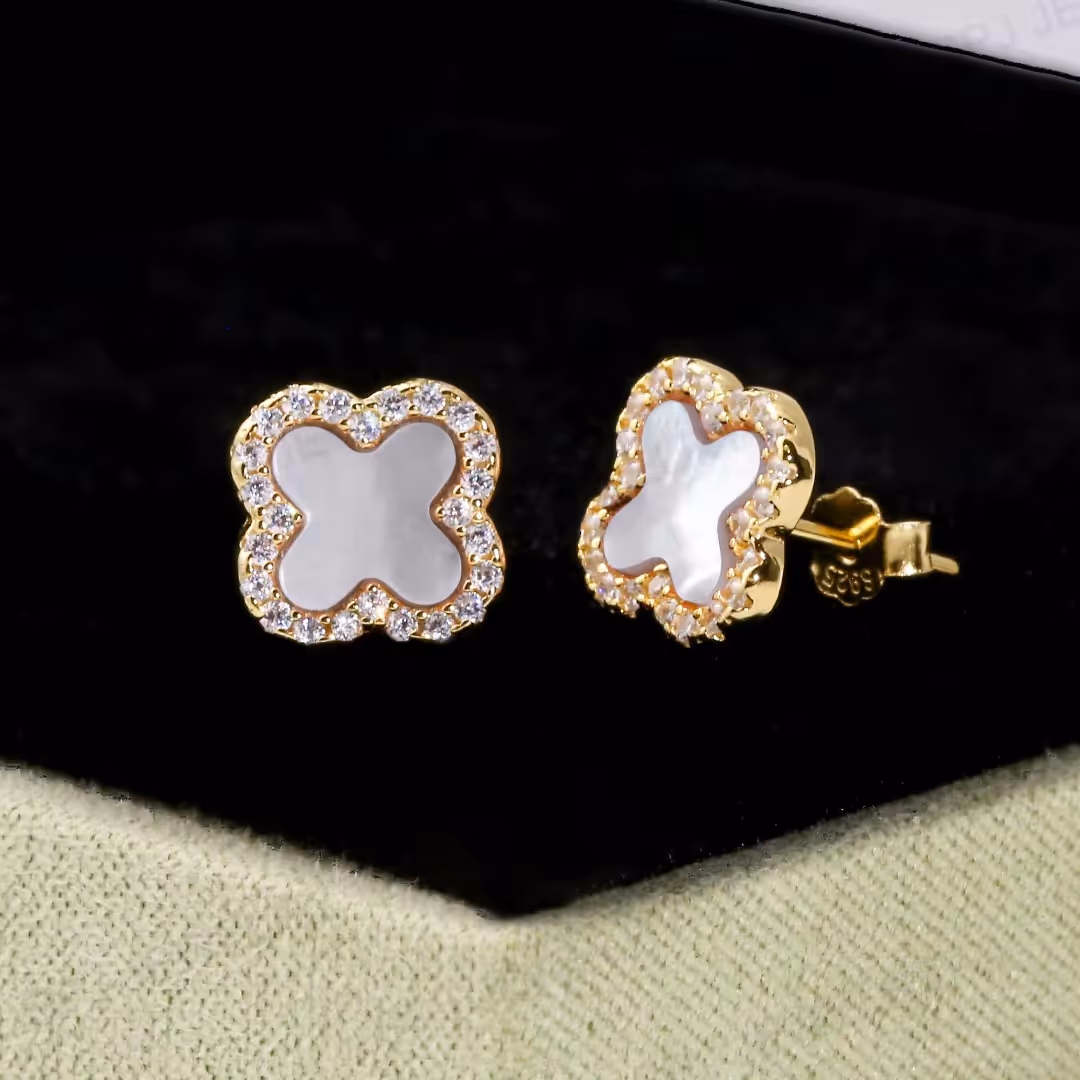 14K gold-plated sterling silver stud earrings with white mother-of-pearl clover centers and cubic zirconia borders displayed on a jewelry stand.