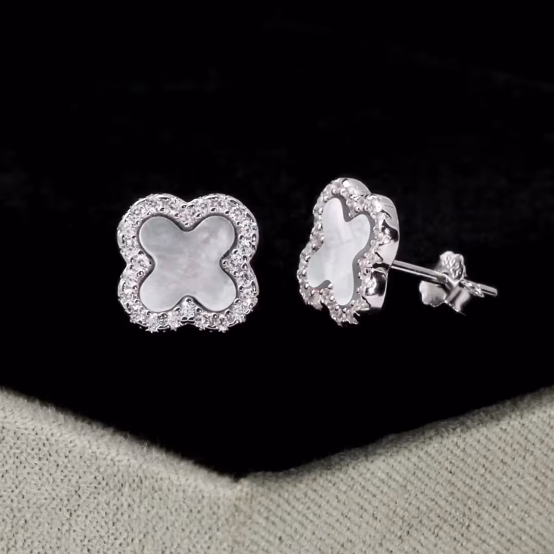 Rhodium-plated sterling silver stud earrings with white mother-of-pearl clover centers and cubic zirconia borders displayed on a jewelry stand.