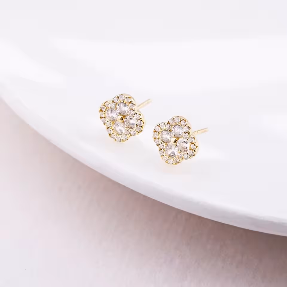Delicate gold floral crystal stud earrings resting on a curved white ceramic surface.