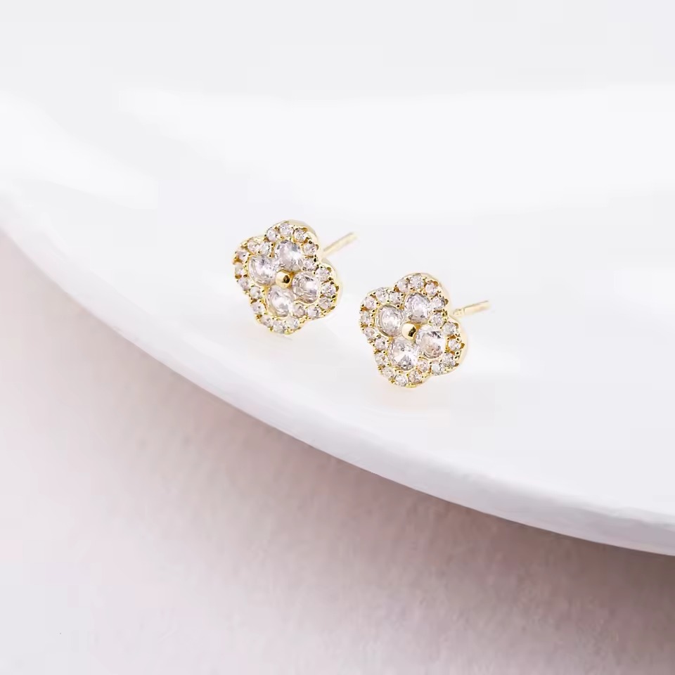 Delicate gold floral crystal stud earrings resting on a curved white ceramic surface.