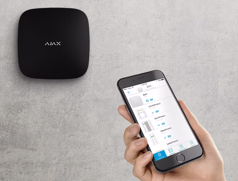 person som holder mobilen mot et innbruddsalarm-panel på veggen