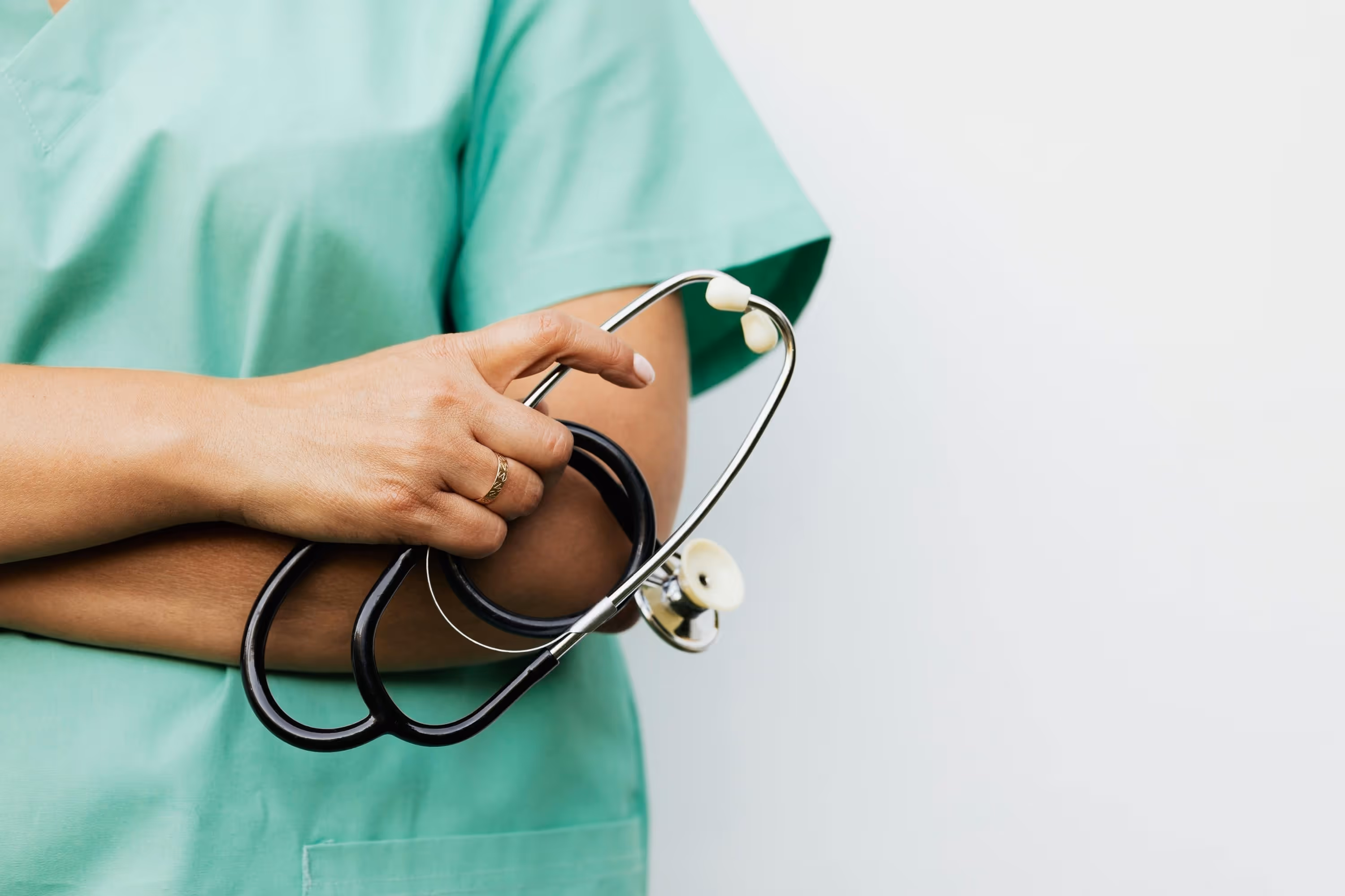 Healthcare professional in green scrubs holding a black stethoscope against a white background.