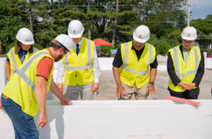 Five construction workers wearing safety vests and helmets inspecting a large white structure outdoors.