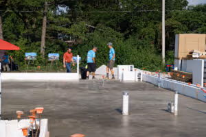 Three workers in safety gear walking on a large concrete slab at a construction site with trees in the background.