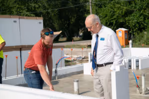 Two men inspecting plumbing pipes at a construction site with white building panels around.