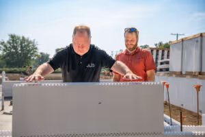 Two men outdoors handling a large, rectangular concrete block at a construction site.