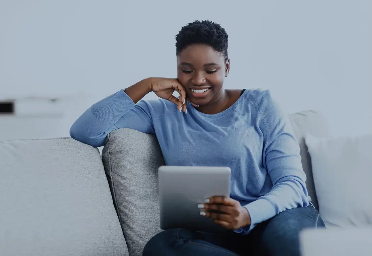 Smiling woman in blue sweater using tablet while relaxing on couch