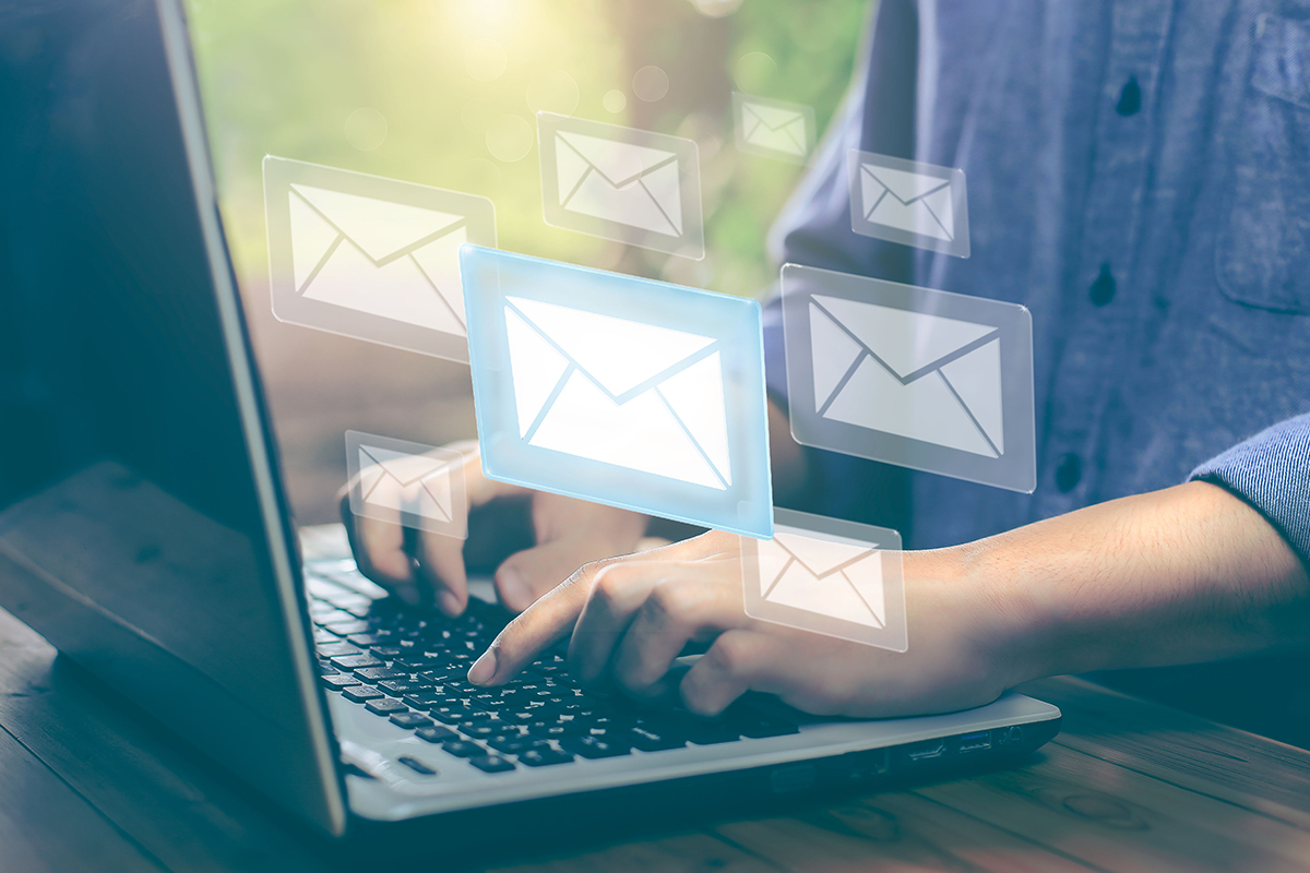 Person sending emails on laptop with floating digital mail icons