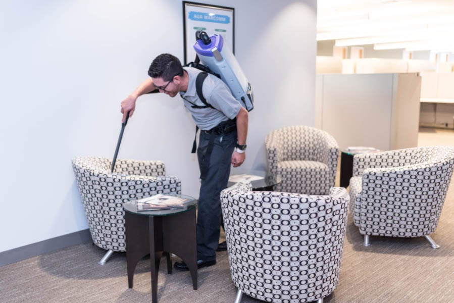 Wooden deck with beige floorboards next to a house wall with textured stone siding and white-framed windows under a copper-colored awning.