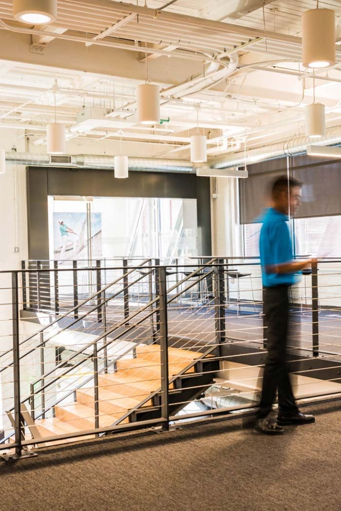 Modern office interior with metal railing stairway and blurred man in blue shirt walking.