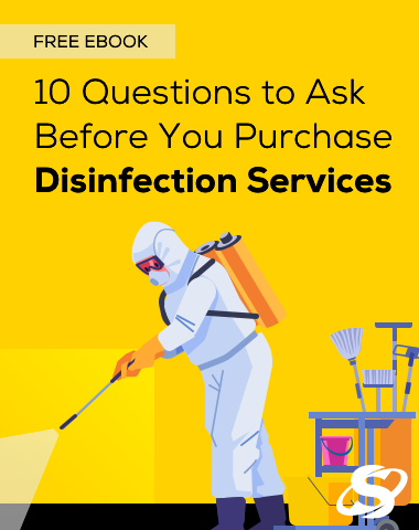 Professional cleaner wearing gloves and uniform wiping a large public restroom sink with a yellow cloth, with cleaning supplies cart nearby.