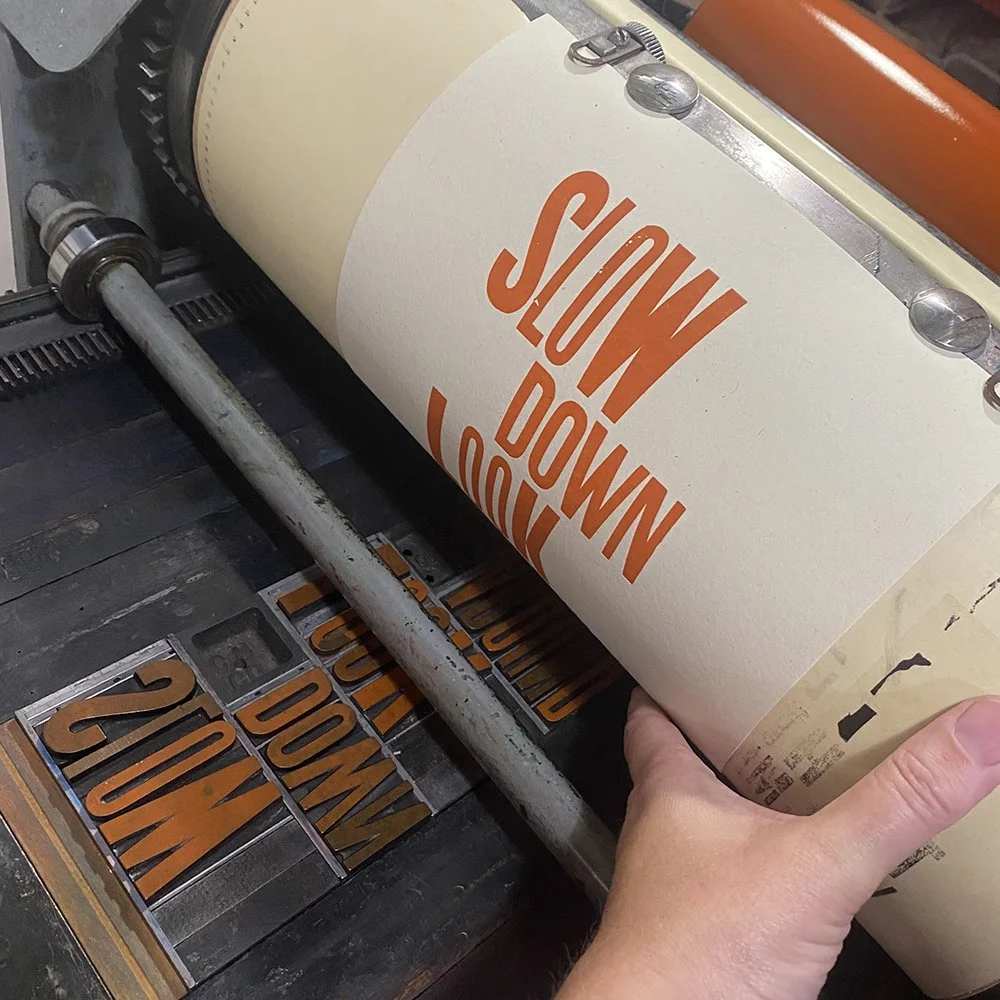 Inked movable metal type set in a letterpress press with the printed paper positioned above it.