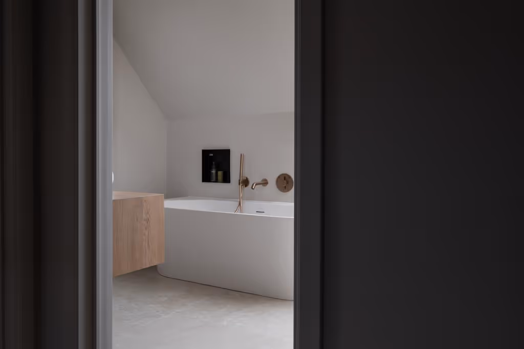 Moderne badkamerrenovatie met een wit bad, gouden kraanwerk en een inbouwnis.