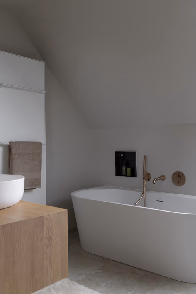 Moderne badkamerrenovatie met een wit bad, gouden kraanwerk en een inbouwnis.