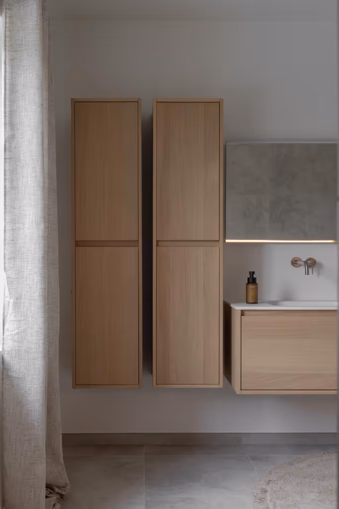 Foto van een luxe badkamerrenovatie met zilveren kraanwerk, strakke spiegel en houten badkamermeubel.