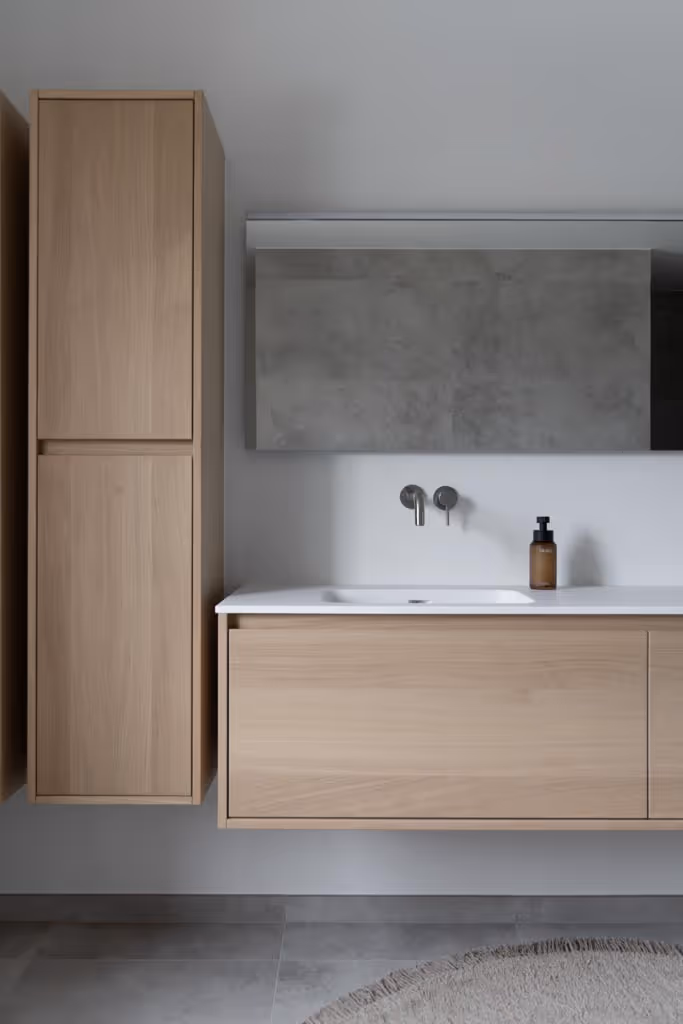 Foto van een luxe badkamerrenovatie met zilveren kraanwerk, strakke spiegel en houten badkamermeubel.