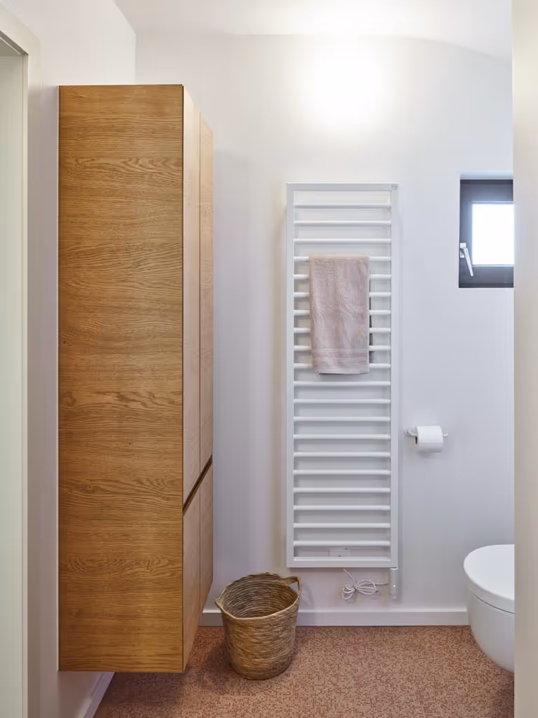 Foto van een badkamerrenovatie met een houten meubel, witte radiator en wit toilet.