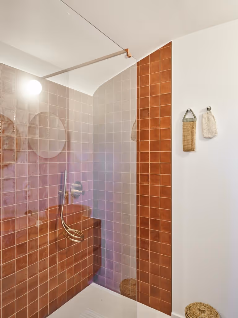 Badkamerrenovatie met glazen douchewand, kleine wandtegels en gouden kranen.