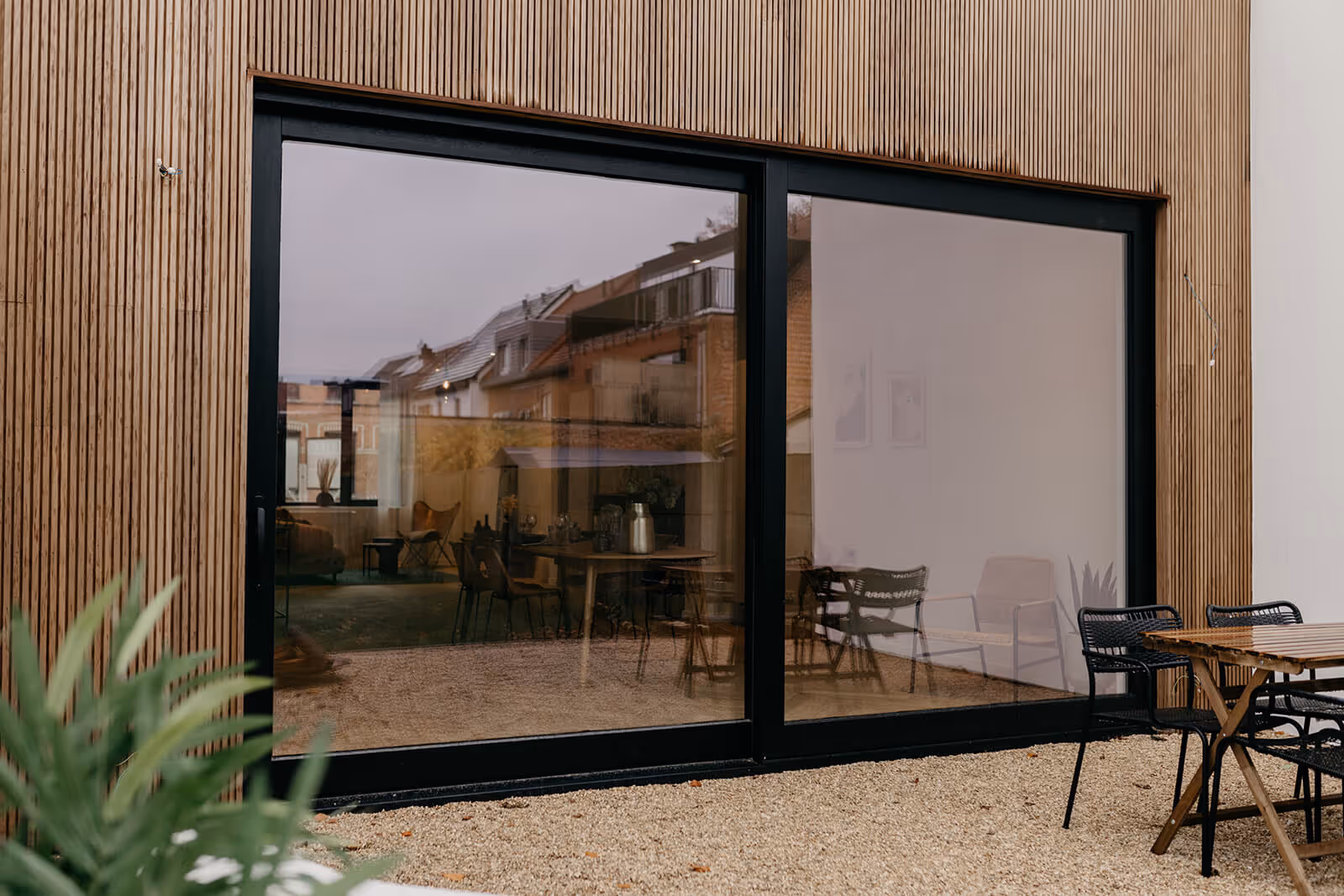 Achtergevel van de renovatie met groot zwart raam, houten gevelbekleding en terras.