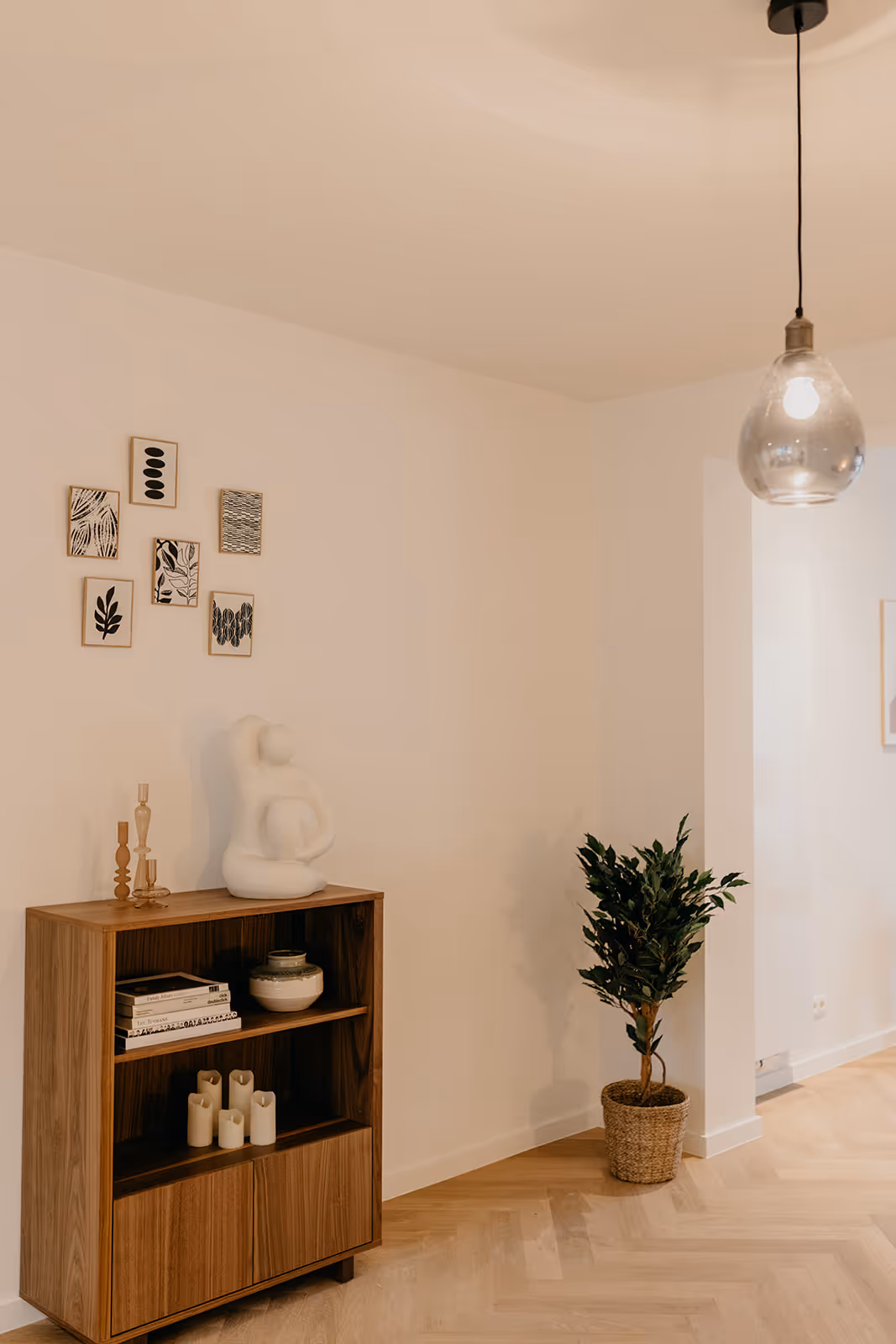 Leefruimte na een totaalrenovatie met open witte ruimte, houten vloer met visgraat parket, en houten meubel.