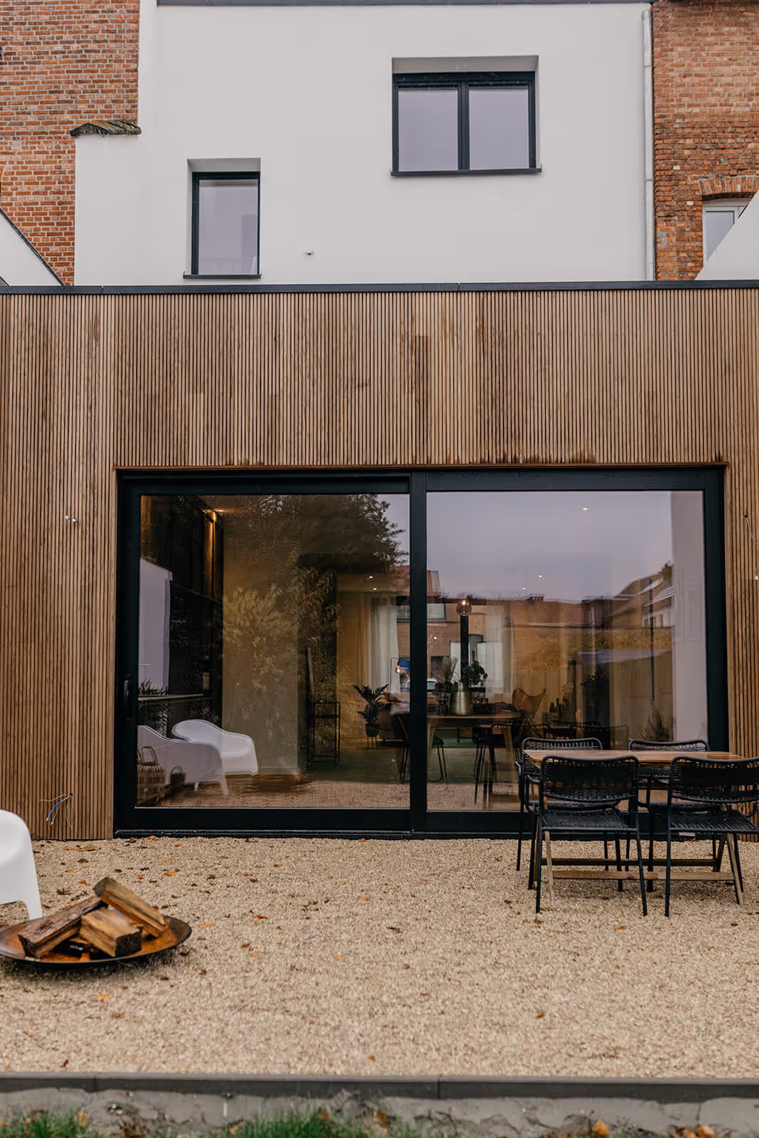 Achtergevel van de renovatie met groot zwart raam, houten gevelbekleding en terras.