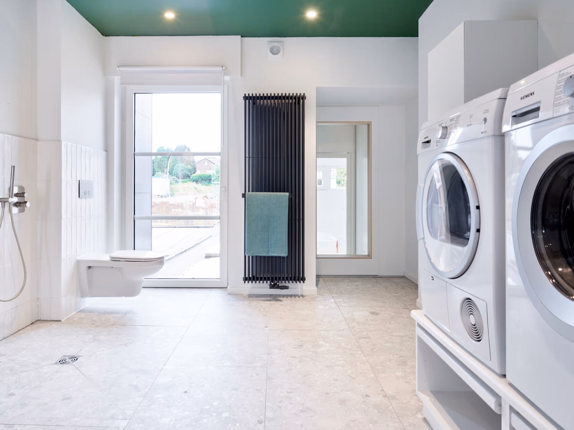 Rolstoeltoegankelijke badkamer na totaalrenovatie met rolstoeltoegankelijk toilet, zwarte radiator en wasplaats.