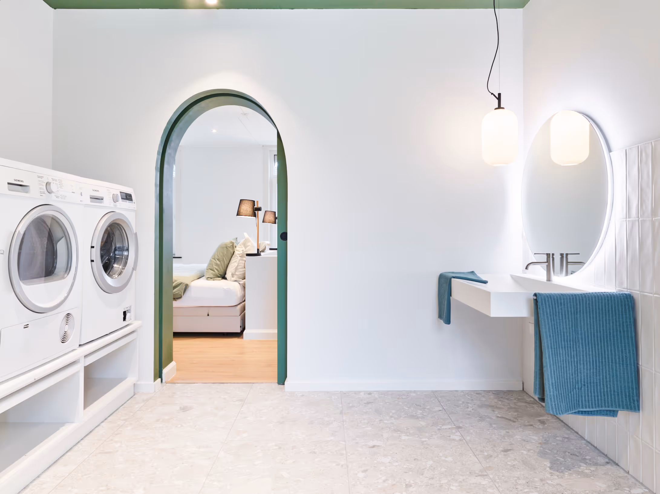 Rolstoeltoegankelijke badkamer met lavabo op hoogte, doorgang naar slaapkamer en wasmachine en droogkast.