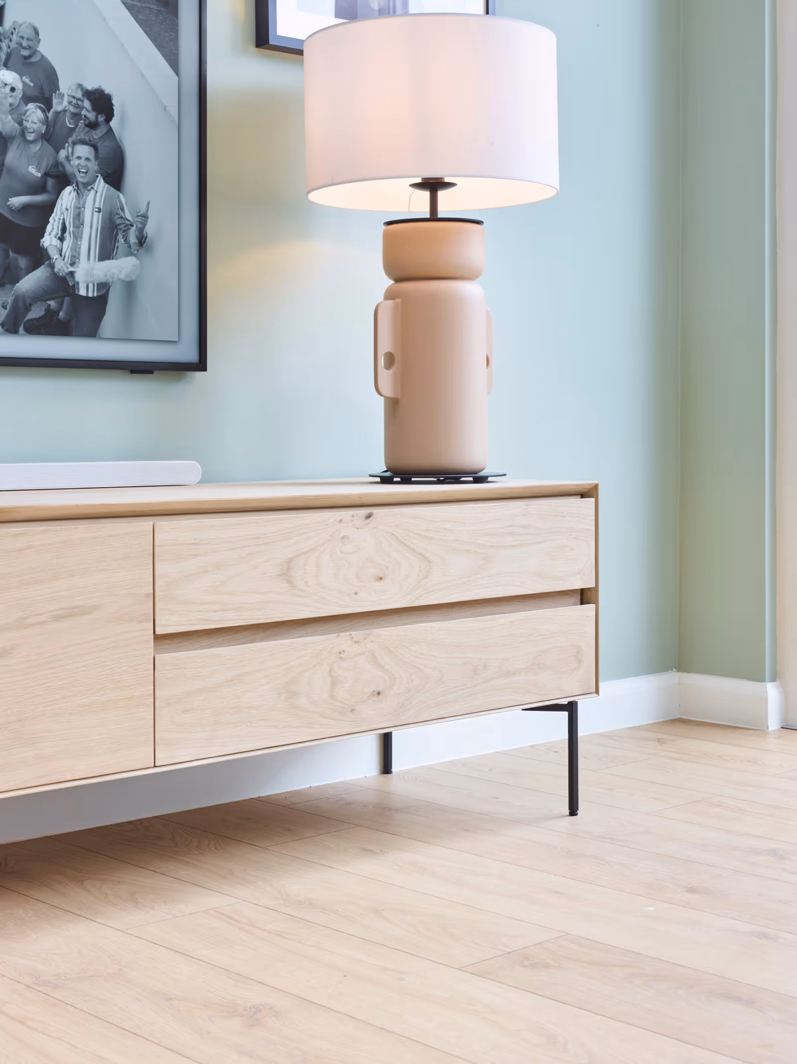 Detail van leefruimte met houten tv-meubel, houten vloer en James Cooke op de achtergrond.